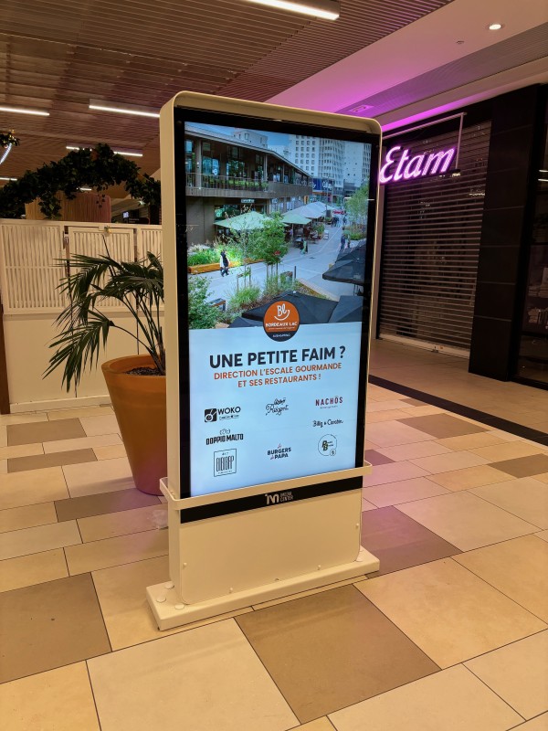 Écrans publicitaires double face installés dans un totem sécurisé au cœur d’une galerie marchande à Bordeaux.
